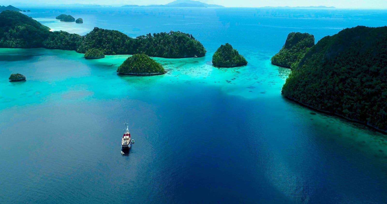 Aerial view of liveaboard vessel surrounded by mushroom-shaped karst islands in Raja Ampat West Papua